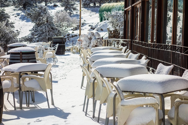 Terrace of a bar after a snowfall with tables and chairs completely covered with snow