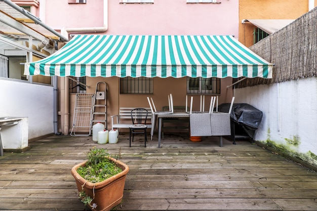 Foto terrazzo patio di una casa al piano terra con alcune piante e pavimento in legno di acacia non verniciato tenda bicolore bianca e verde e portico di accesso