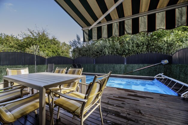 Terras met overdekt zwembad van een eengezinswoning met vloer van akaciehout buiten eettafel met bijpassende stoelen en intrekbare luifel op het dak