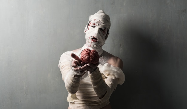 Photo terrorific mummy eating a brain on textured wall background.  halloween holidays