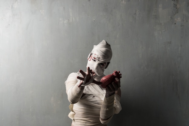 Photo terrorific mummy eating a heart on textured wall background.  halloween holidays