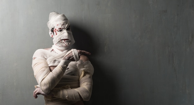 Foto terrorifice mummie die aan de zij op geweven muurachtergrond richt. halloween vakantie