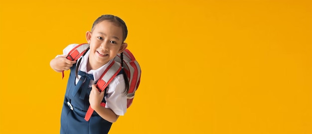 Terug naar school banner idee concept Gelukkig Aziatisch schoolmeisje in uniform geïsoleerd op gele achtergrond met uitknippaden voor ontwerpwerk leeg