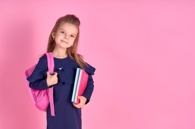 Terug naar school concept half gedraaide foto portret van mooie zelfverzekerde mooi slim meisje met schrift notebook dragen schooluniform jurk roze heldere rugzak geïsoleerd