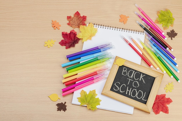 Terug naar school concept Herfstbladeren schoolbord met tekst Zakelijke achtergrond met kantoorbenodigdheden houten tafel plat bovenaanzicht