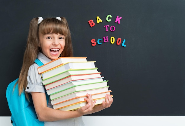 Terug naar school concept Leuke leerling met boeken aan het zwarte schoolbord in het klaslokaal