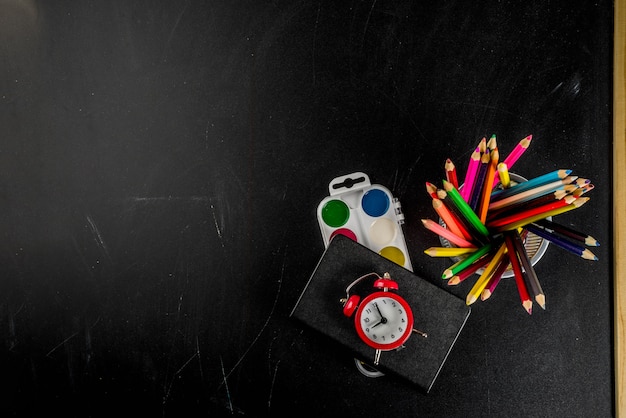 Terug naar school concept met boeken wekker kleur potloden schoolbord achtergrond