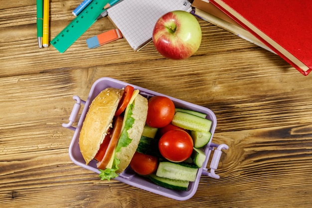 Foto terug naar school concept school levert boeken appel en lunchbox met hamburgers en verse groenten op een houten tafel bovenaanzicht