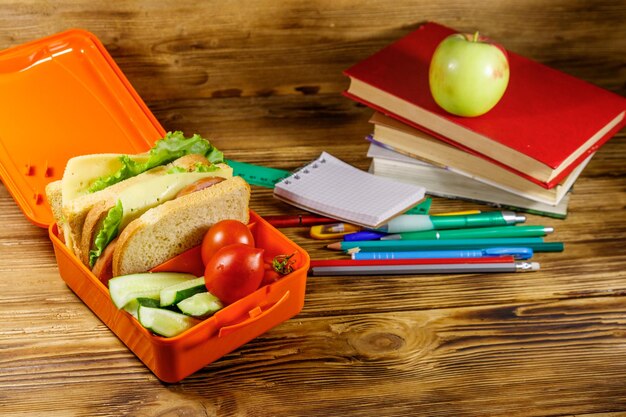 Terug naar school concept School levert boeken appel en lunchbox met sandwiches en verse groenten op een houten bureau