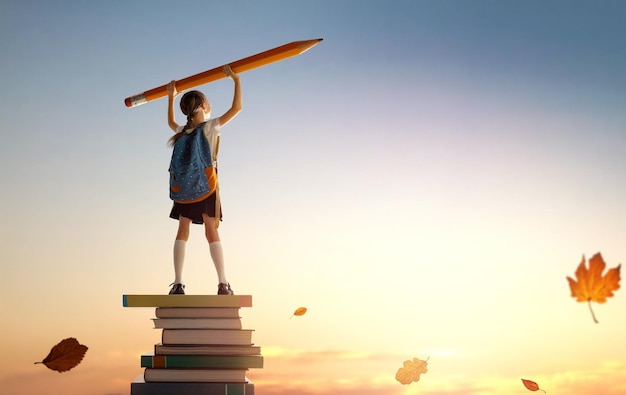 Foto terug naar school gelukkig schattig ijverig kind staat op de toren van boeken en houdt een enorm potlood vast