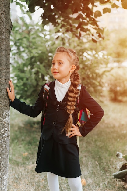 Terug naar school, klein gelukkig kind leerling schoolmeisje acht jaar oud in mode-uniform met rugzak en kapsel volumineuze lange vlecht klaar naar de eerste dag van de tweede klas op de basisschool flare