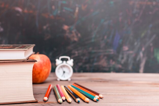 Foto terug naar school met boeken, potloden, klok en appel op woodtable over bord