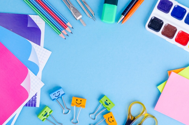 Terug naar school met scholenaccessoires - verven, potloden, notitieboekjes, schaar, tellers, blauwe achtergrond.