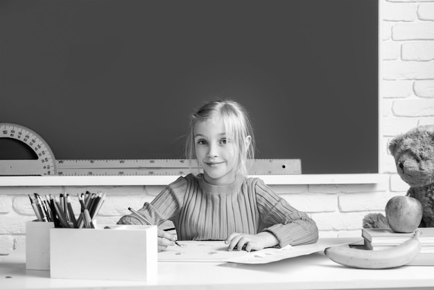 Terug naar school Schattige leerling meisje tekenen aan de balie Kind in de klas met schoolbord op achtergrond Onderwijs leren en kinderen concept