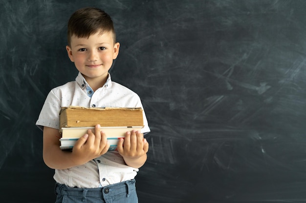 Terug naar school Schooljongen jongen permanent met boeken op de achtergrond van een zwart krijtbord met een plek voor tekst Faculteit student slim kind in de klas Onderwijs en scholing