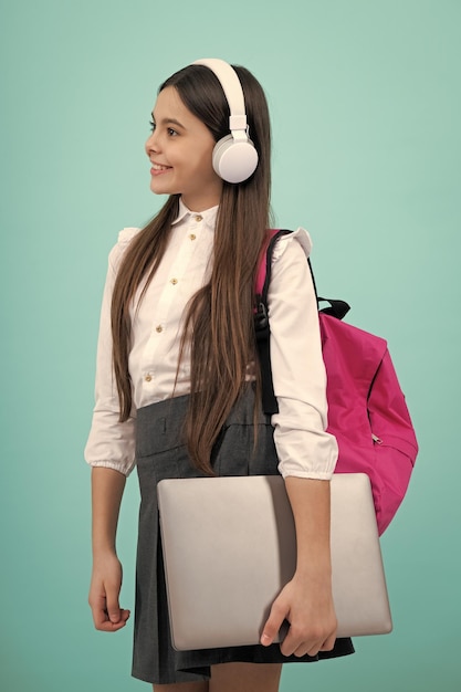 Terug naar school Tiener schoolmeisje in schooluniform met rugzak koptelefoon en laptop Schoolkinderen op geïsoleerde blauwe achtergrond