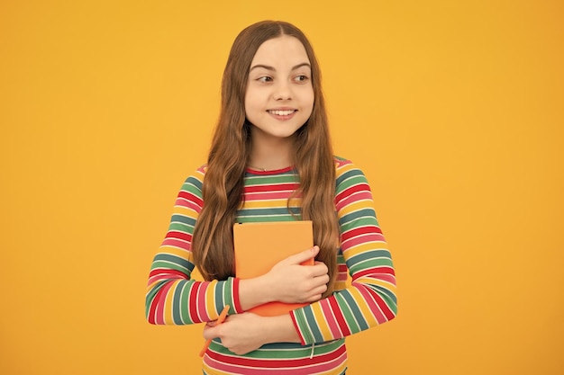 Foto terug naar school tienerschoolmeisje met boek klaar om te leren schoolmeisjeskinderen op geïsoleerde gele studioachtergrond