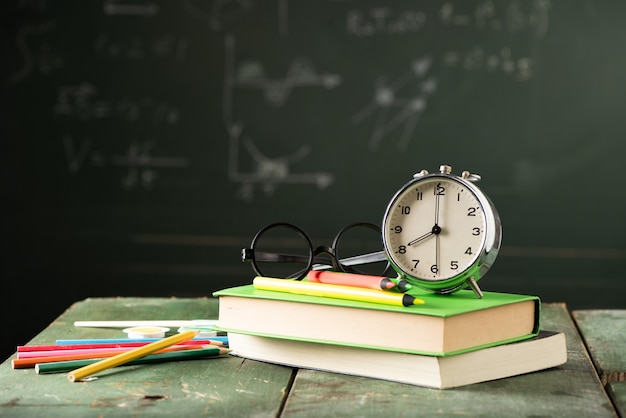 Terug naar schoolachtergrond met boeken en wekker over bord. Terug naar schoolconcept