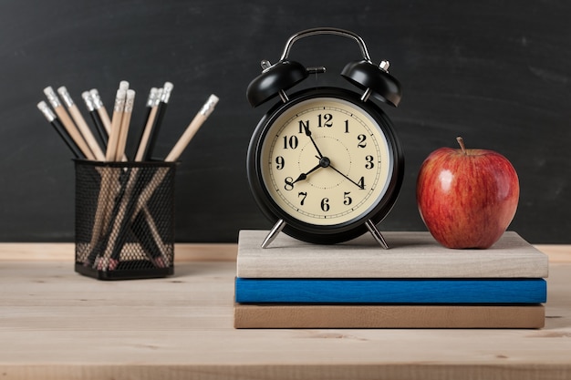 Terug naar schoolachtergrond met wekker, appel en potloden op bordachtergrond