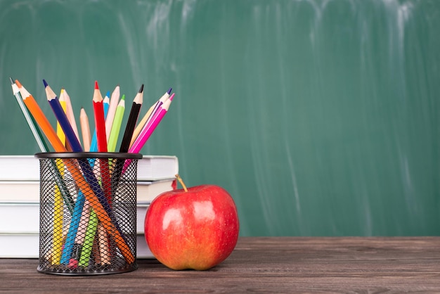 Terug naar schoolconcept. Close-up foto van kleurrijke kleurpotloden rode appel en leerboeken geïsoleerd op groen schoolbord