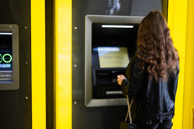 Terug van jong donkerbruin meisje dat geld van creditcard opneemt bij gele ATM