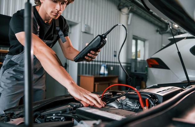 Test auto-elektronica Volwassen man in grijs gekleurd uniform werkt in de autosalon