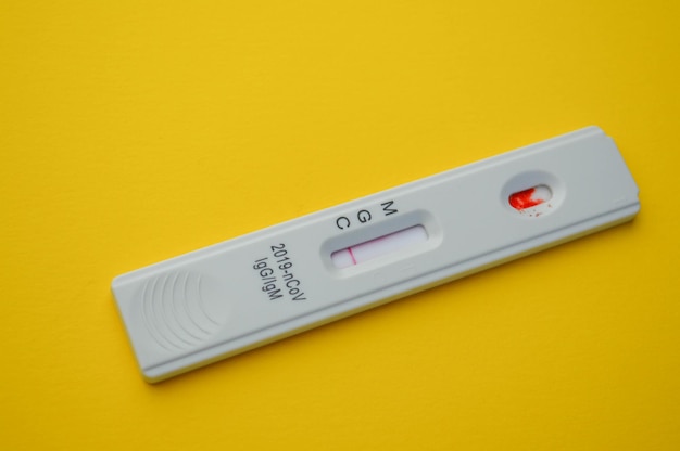 Foto il test per il coronavirus si trova su uno sfondo giallo una goccia di sangue su una diagnosi rapida della striscia reattiva