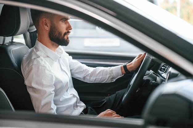 Test drive Young man in white clothes is in the car dealership
