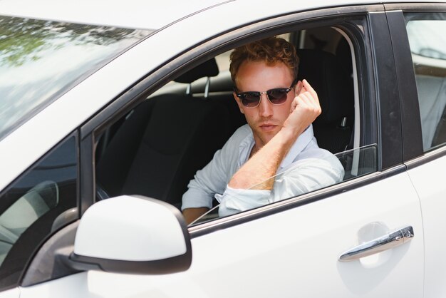 Test driving of new generation electro vehicle with self driving system. Handsome Caucasian man sitting behind the wheel of new modern car and smiling at camera.