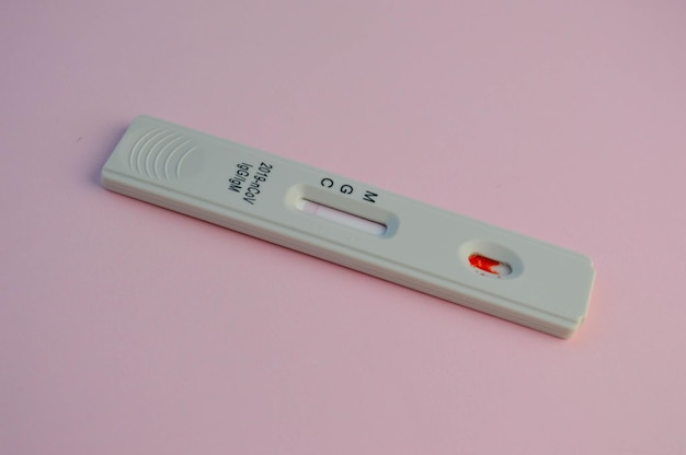 Фото Тест на коронавирус лежит на розовом фоне, на тест-полоске экспресс капля крови