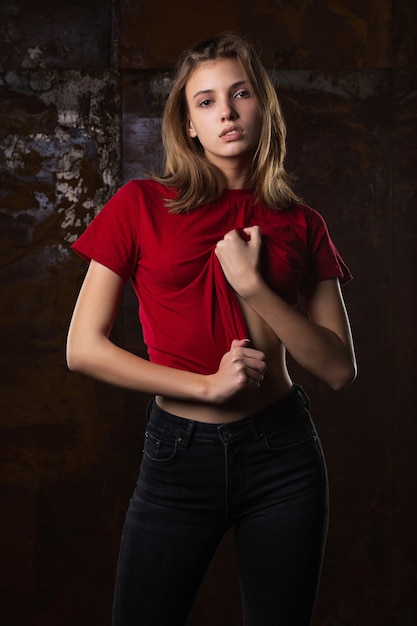 Test shoot of glamor young model posing in t shirt and jeans against grey wall