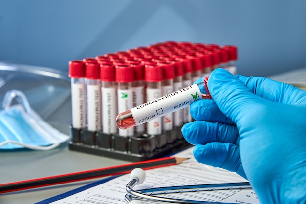 Photo a test tube in hand with negative blood samples for covid-19 next to the coronovirus test form.