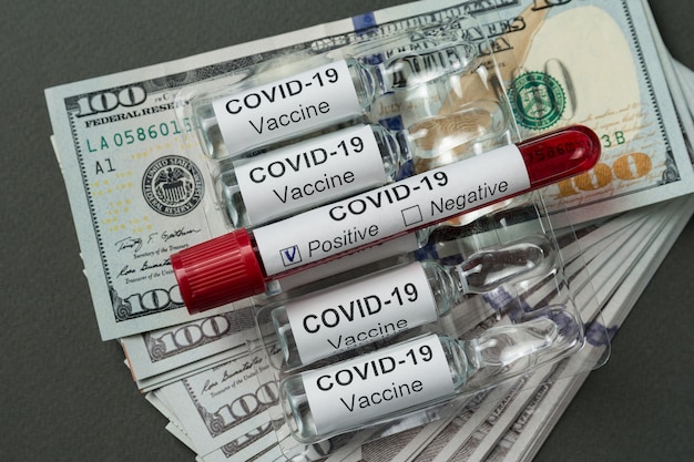 Test tube with blood for Covid-19 analyzing. Ampoules of vaccine are on stack of dollars.