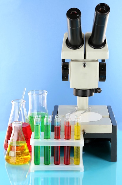 Пробирки с красочными жидкостями и микроскопом на синем фоне