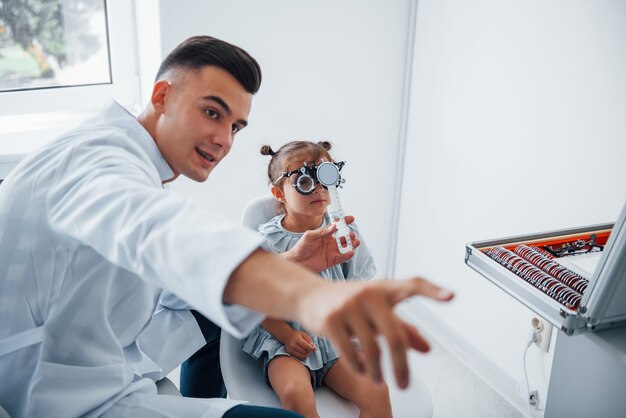 Testing vision. Young ophthalmologist is with little female visitor in the clinic.