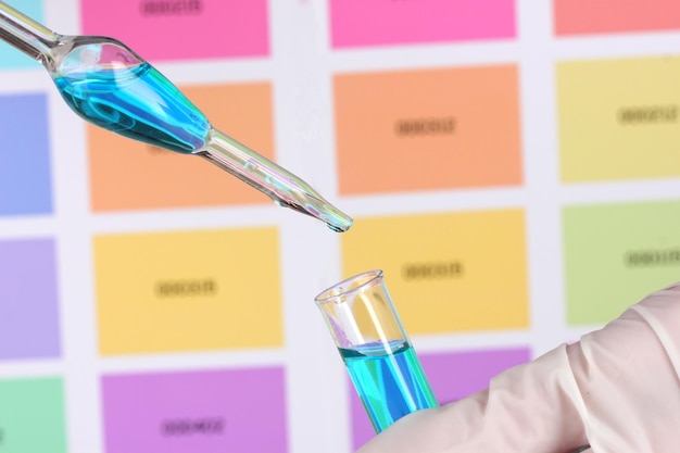 Foto provetta con liquido blu e pipetta nelle mani dello scienziato su sfondo di campioni di colore