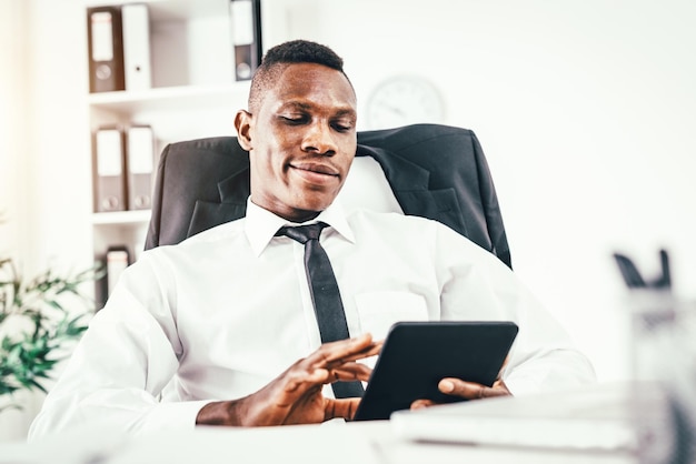 Tevreden Afrikaanse zakenman die aan digitale tablet in modern bureau werkt.