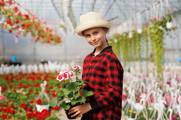 Tevreden dochter van tuinman die naar de camera kijkt en glimlacht met een potplant in de hand.