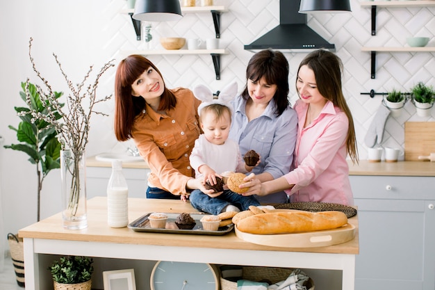 Tevreden familie met oma, twee dochters en een klein meisje genieten van tijdverdrijf op pasen en het eten van cupcakes. een klein meisje heeft konijnenoren op haar hoofd.