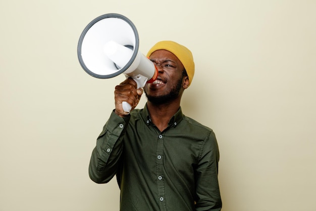 Tevreden jonge Afro-Amerikaanse man in hoed met groen shirt spreekt op luidspreker geïsoleerd op een witte achtergrond