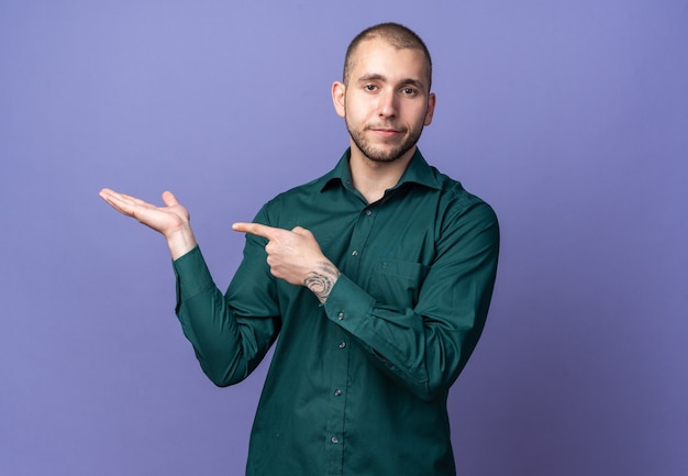 Tevreden jonge knappe kerel met een groen shirt die doet alsof hij vasthoudt en wijst naar iets