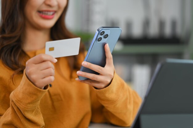 Tevreden jonge vrouw met een creditcard die online betalingen maakt op haar mobiele telefoon