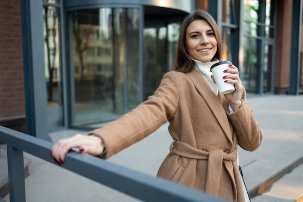 Tevreden jonge vrouw met papieren kopje koffie buiten