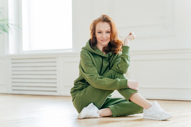 Tevreden jonge vrouw met rood haar in goede lichaamsvorm doet yoga rekoefeningen versterkt spieren gekleed in sportkleding houdt fit heeft een gezonde levensstijl Mensen en sportconcept