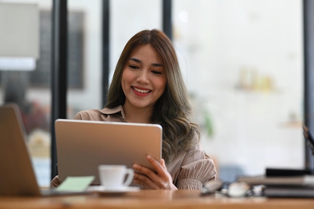 Tevreden jonge zakenvrouw die digitale tablet gebruikt op modern kantoor
