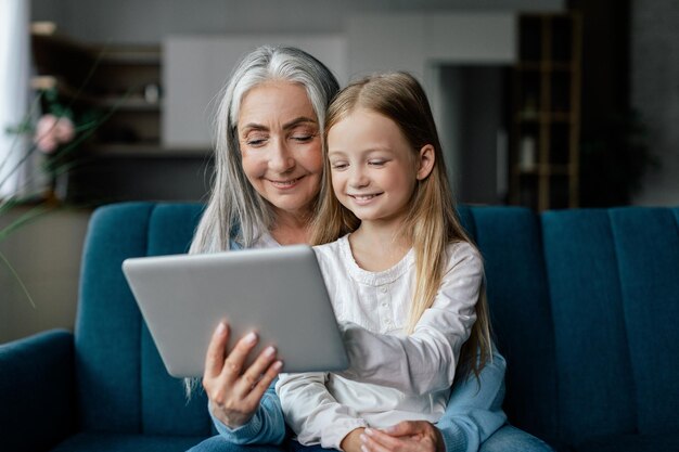 Tevreden kaukasisch klein meisje en oude dame bekijk video geniet van online game op tablet bel op de bank