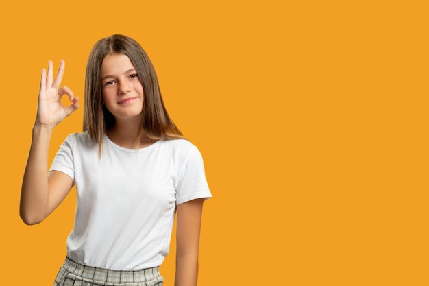 Tevreden kind reclame achtergrond perfecte keuze goedkeuring teken portret van vrolijk gelukkig meisje in het wit weergegeven: OK gebaar glimlachend geïsoleerd op oranje lege ruimte