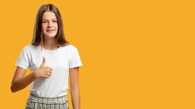 Tevreden kind reclame achtergrond perfecte keuze goedkeuring zingen portret van gelukkig vrolijk meisje in witte tshirt duim opdagen als gebaar glimlachend geïsoleerd op oranje kopie ruimte