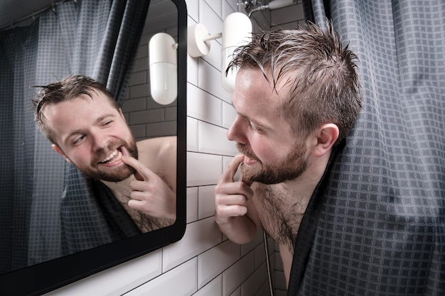 Tevreden knappe man opende mond en bekeek zorgvuldig zijn mooie gezonde tanden in de spiegel