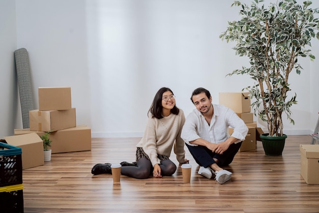 Tevreden lachende geliefden zittend op houten vloer dicht bij elkaar in nieuw gehuurde apartament
